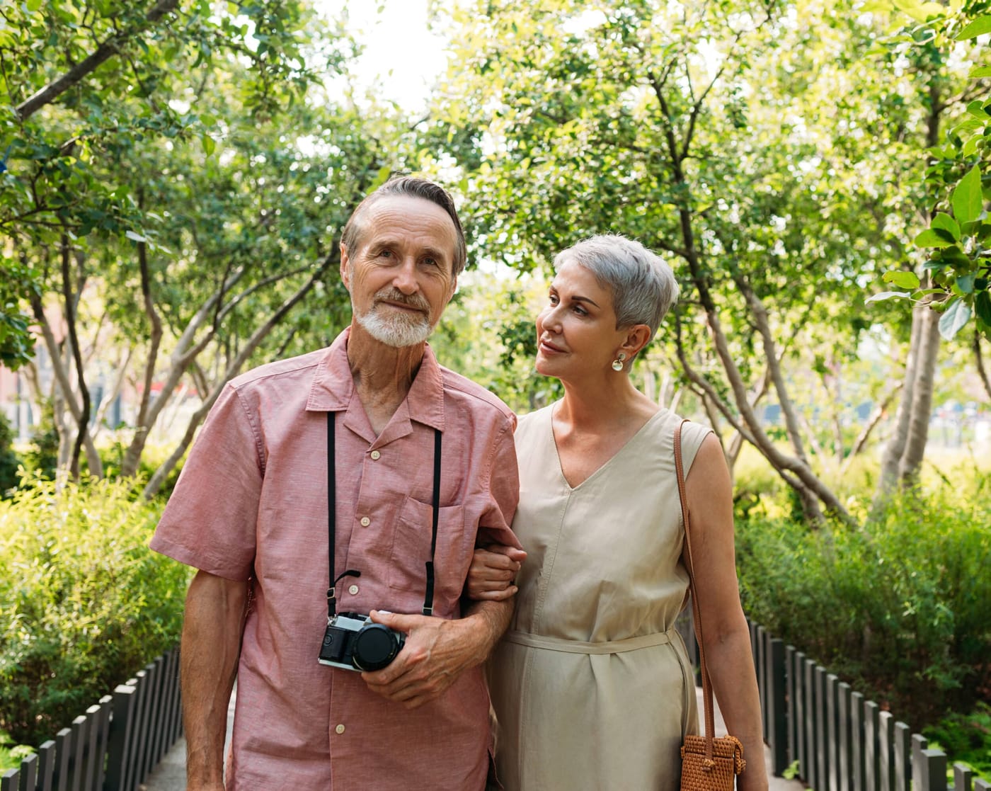 Una pareja mayor camina por un sendero de jardín; uno de los dos lleva una cámara
