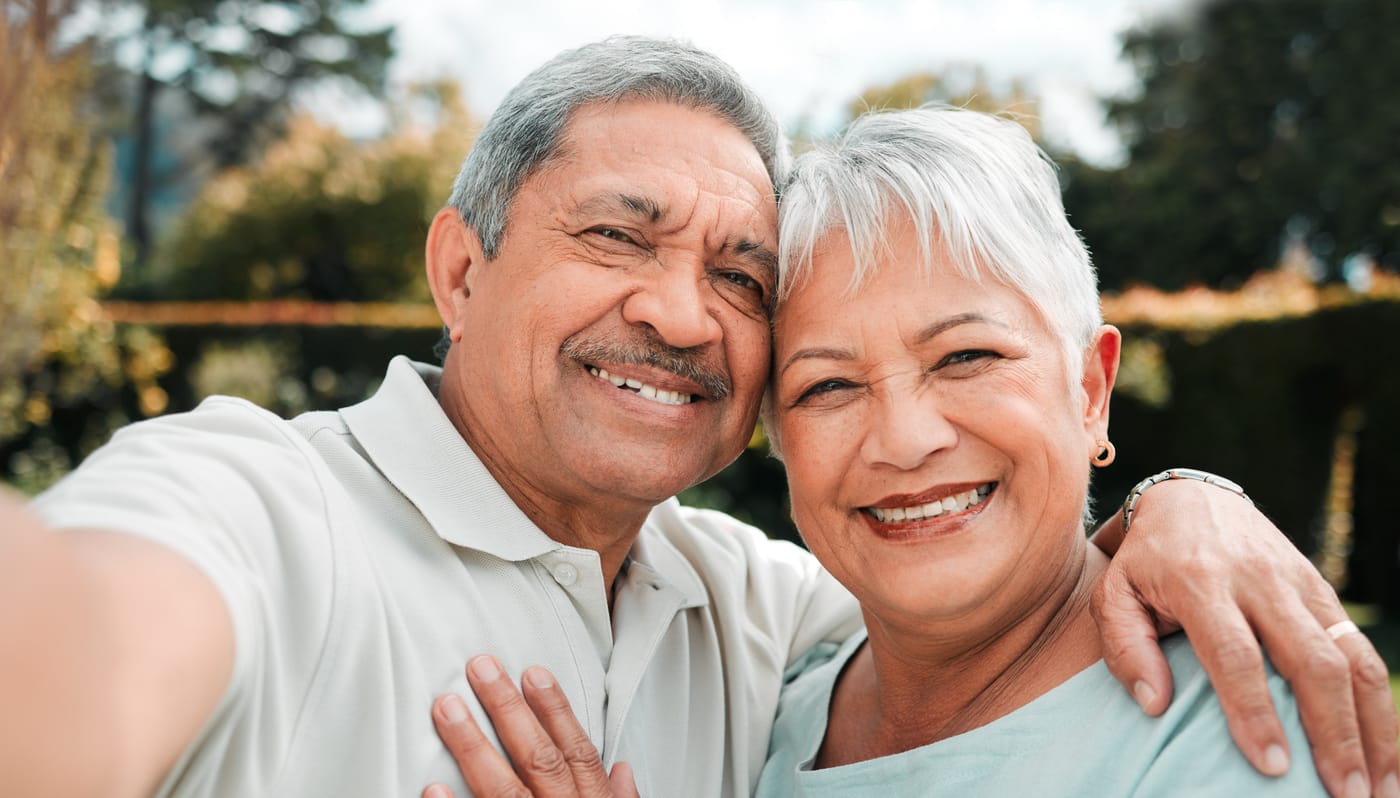 Una pareja de adultos mayores sonriente se toma una selfi al aire libre