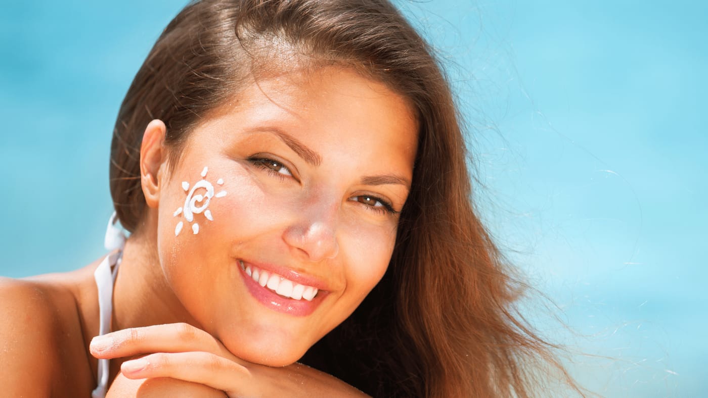 A smiling woman with a sun drawn in sunscreen on her cheek