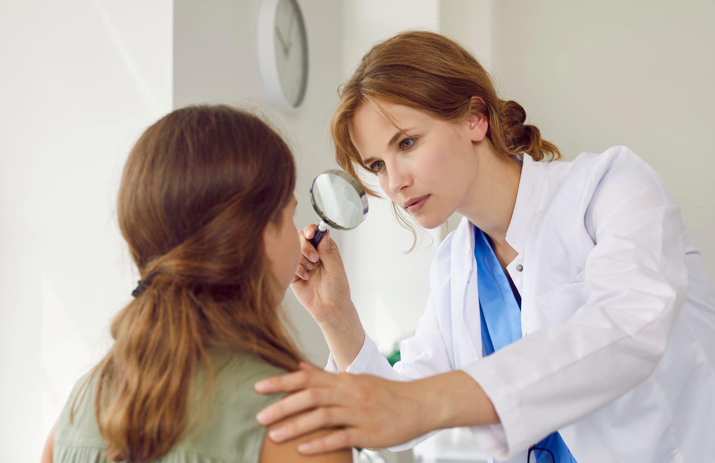 A dermatologist examines a teenage girl's facial skin with a magnifying glass