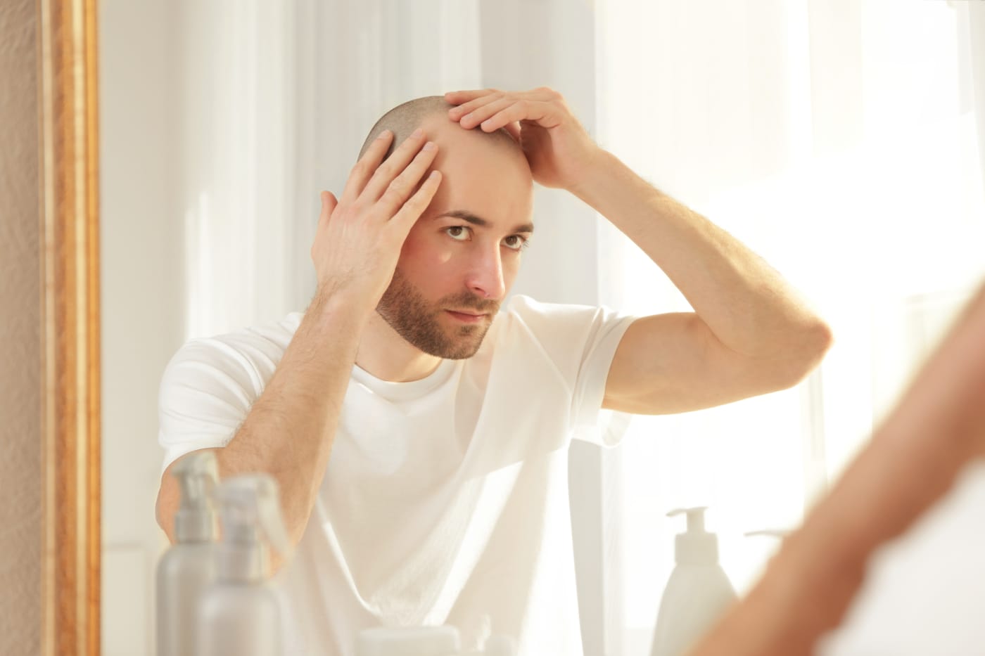 A young man checks his thinning hairline in a bathroom mirror
