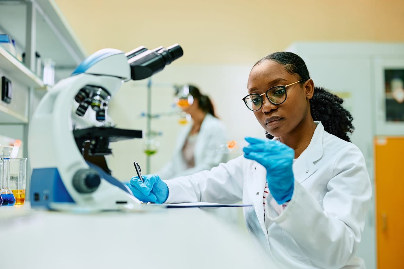 A researcher in safety glasses examines a sample on a microscope slide in a laboratory