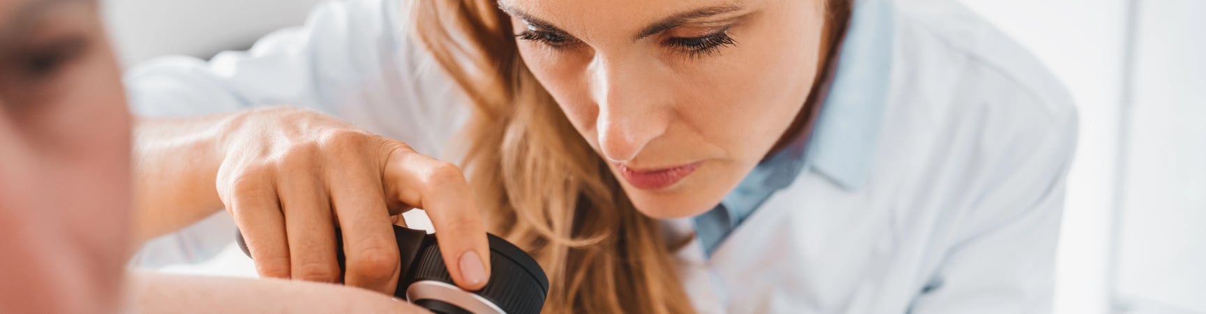 A dermatologist examines a patient's skin through a dermatoscope